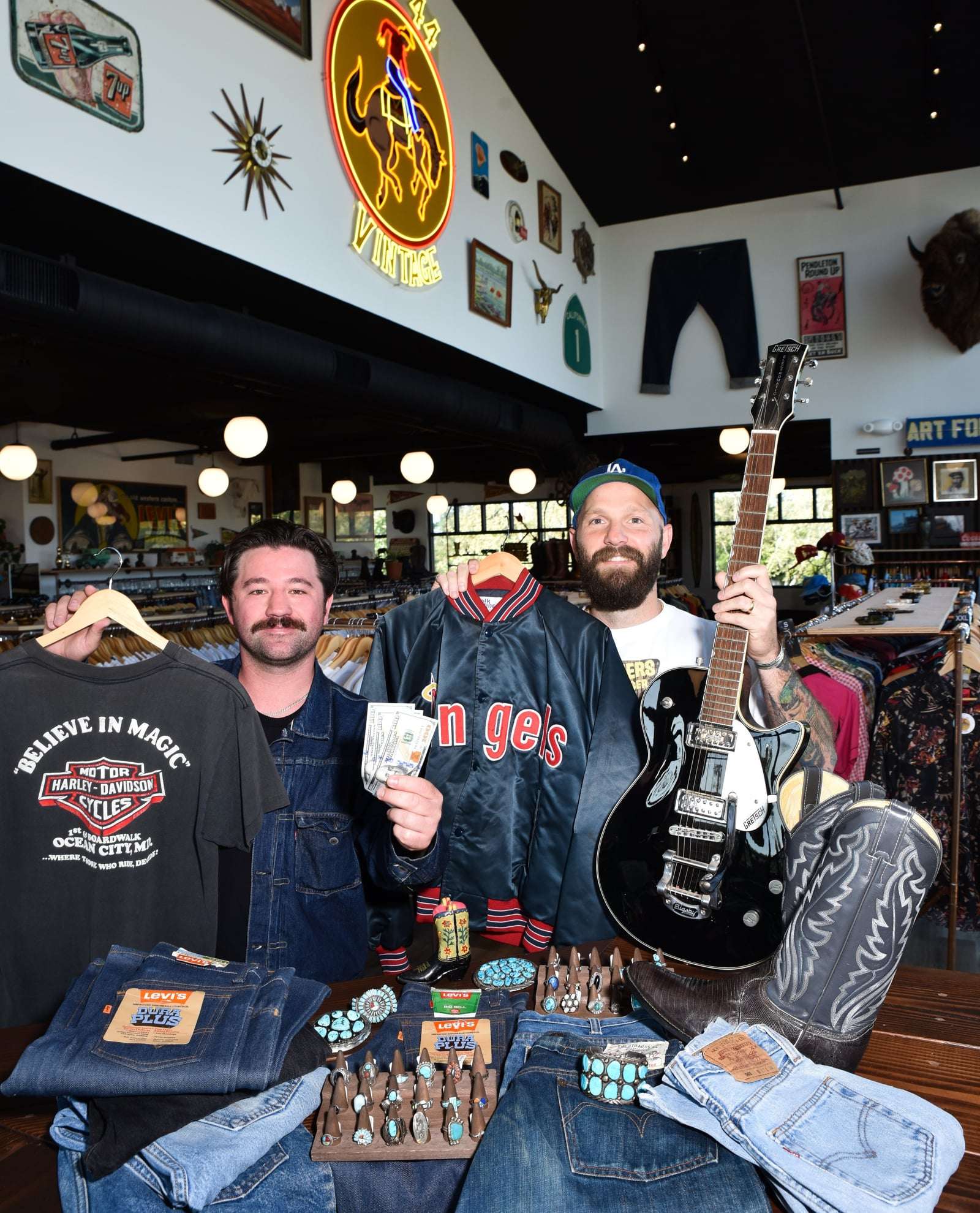 Sam and Jake of Old 44 Vintage holding vintage denim, a Gretsch guitar, and an Angels jacket, surrounded by turquoise jewelry and Levi's